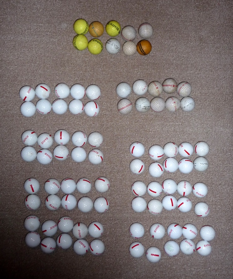 Rows of range balls laid out on a dark surface, most of them white with a few coloured ones at the top.
