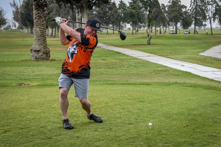 A golfer in an orange shirt partway through the downswing on an open course, hands still above waist height.