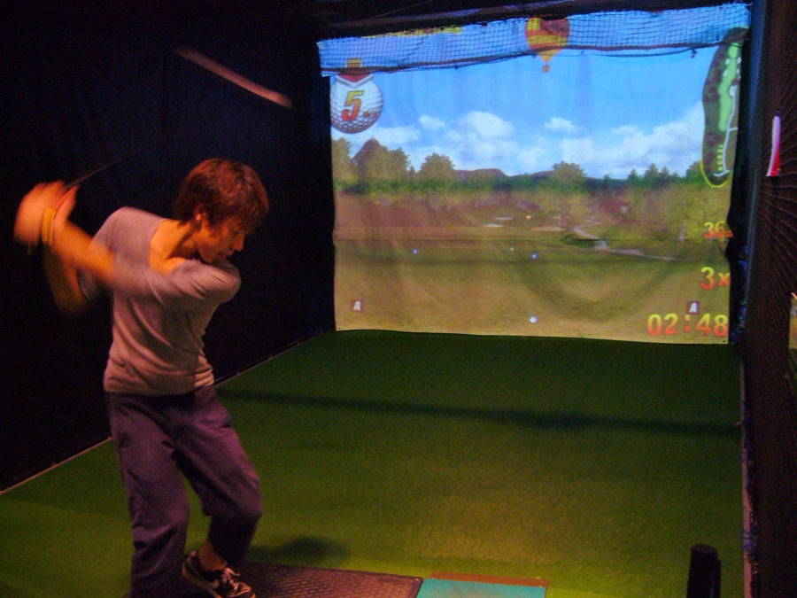 A golfer hitting into an indoor simulator screen, the projected fairway lit up in front of them.