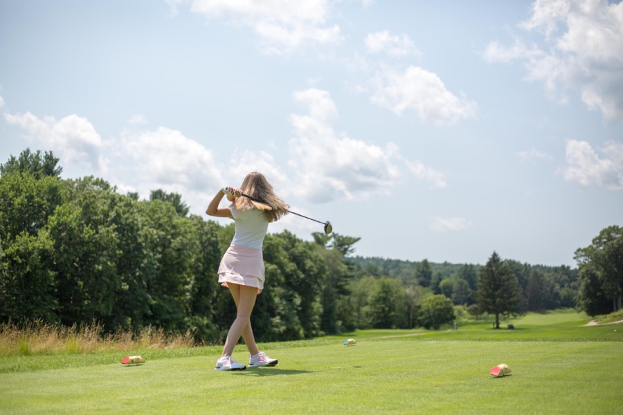 A golfer photographed from behind on the target line partway into the downswing, hips and lower back visible against the fairway.
