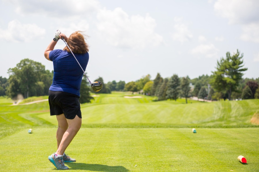 A golfer just past the top, seen from behind along the target line, hips turning toward the target while the club is still high.