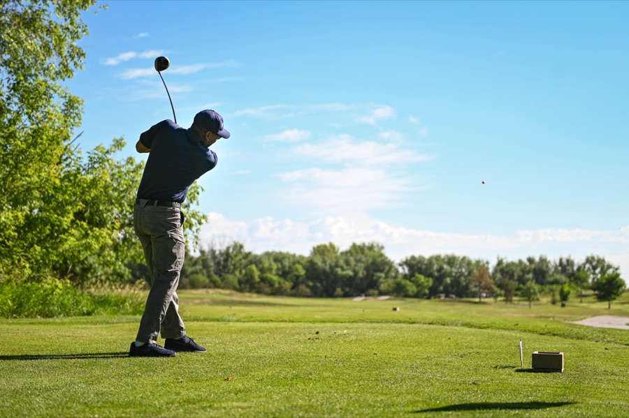 A golfer photographed from behind on a wide fairway, club above the shoulders against an open blue sky.