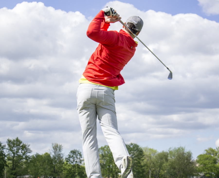 A golfer in a red top swinging on a course, weight and chest turning through under a cloudy sky.
