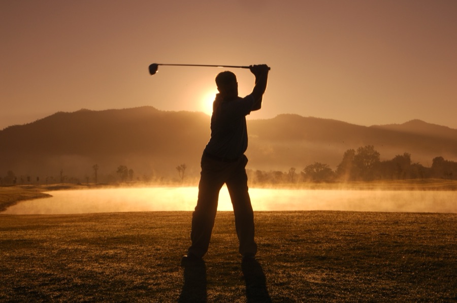 A golfer photographed from the side partway through the downswing, hips already turning toward the target while the hands are still above waist height.