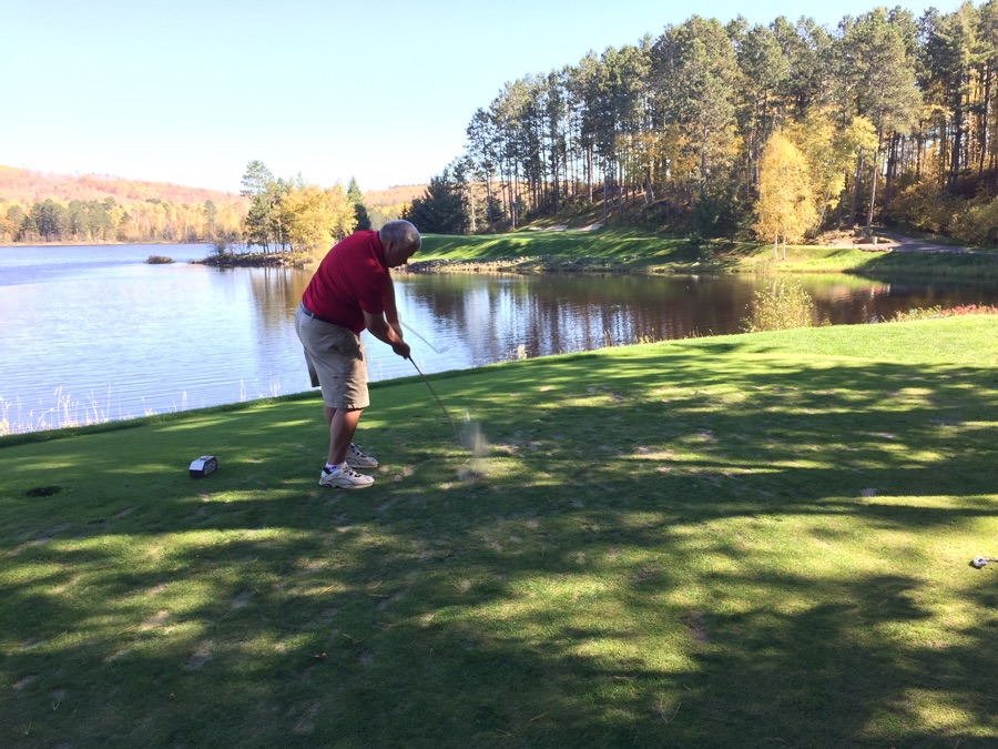 A right-handed golfer photographed from behind on the target line, midway through the downswing with the club still above shoulder height.