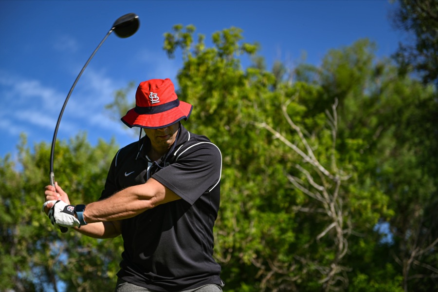 A golfer mid-swing at a charity tournament, the fairway and trees running away behind.