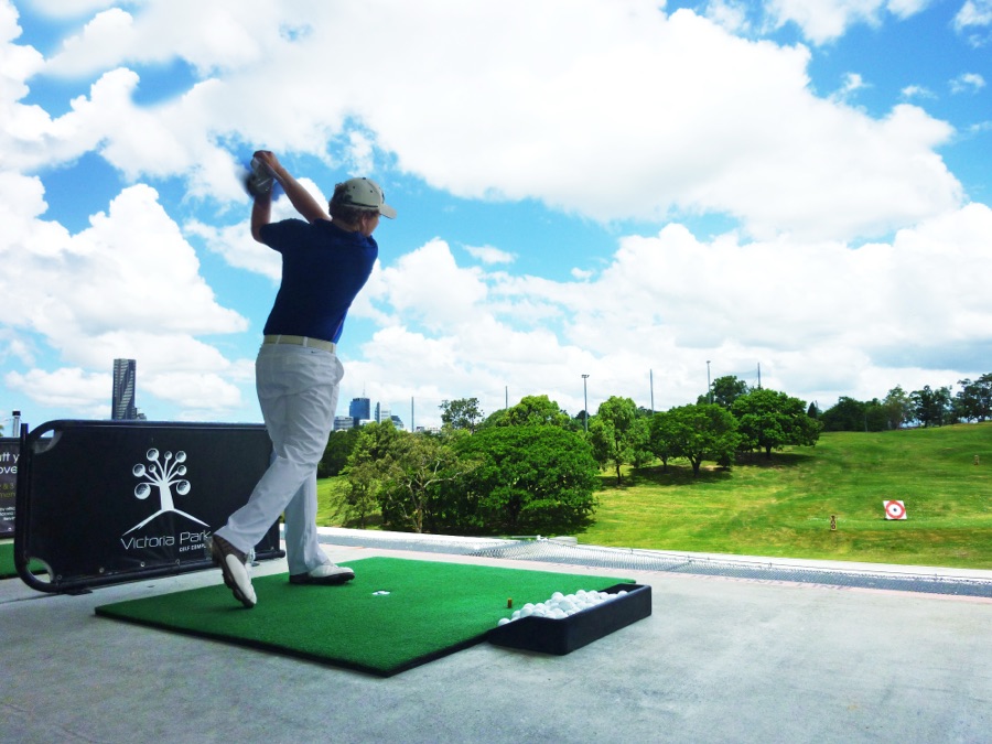 A golfer on a driving range mat at the top of the backswing, photographed from behind along the target line.